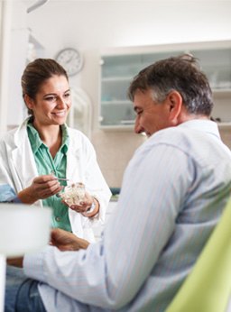 Smiling dentist showing patient model of teeth